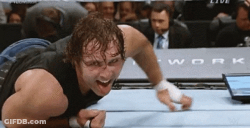 A Wrestler Is Laying On The Floor With His Mouth Open In A Wrestling Ring GIF