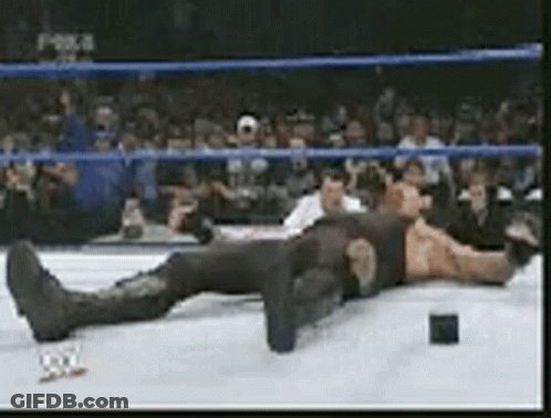A Wrestler Is Laying On The Ground In A Wrestling Ring . GIF