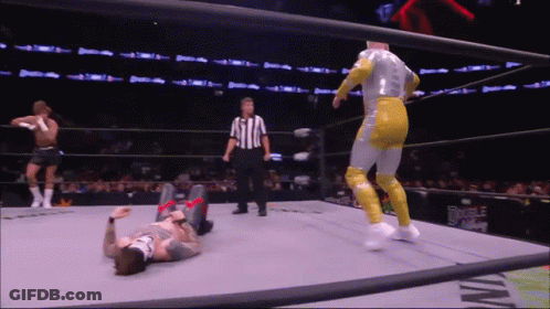 A Wrestler Is Laying On The Ground In A Wrestling Ring While A Referee Watches GIF