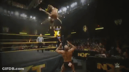 A Wrestler Is Laying On The Ground In Front Of A Sign That Says Nxt On It GIF