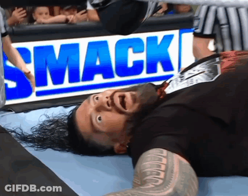 A Wrestler Is Laying On The Ground In Front Of A Smack Sign GIF