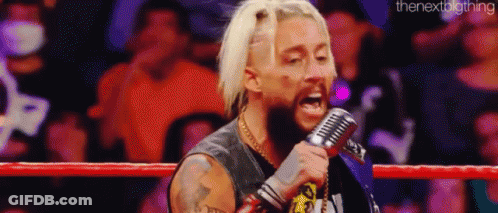A Wrestler Is Singing Into A Microphone While Standing In A Boxing Ring . GIF