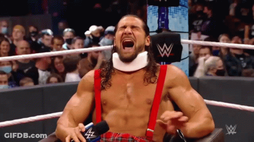 A Wrestler Is Sitting In A Chair With His Mouth Open And A Microphone In His Hand . GIF