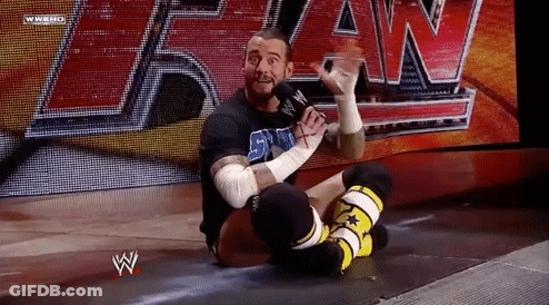 A Wrestler Is Sitting On The Floor With A Microphone In His Hand . GIF