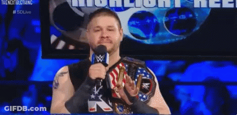 A Wrestler Is Speaking Into A Microphone While Wearing A Wwe Championship Belt . GIF