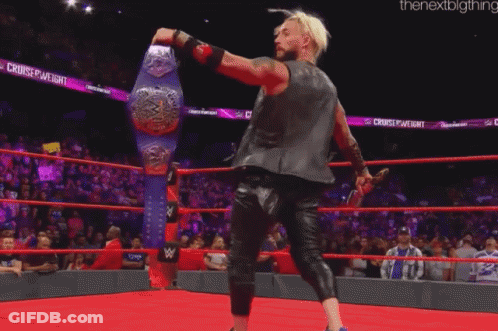 A Wrestler Is Standing In A Ring Holding A Wrestling Championship Belt GIF