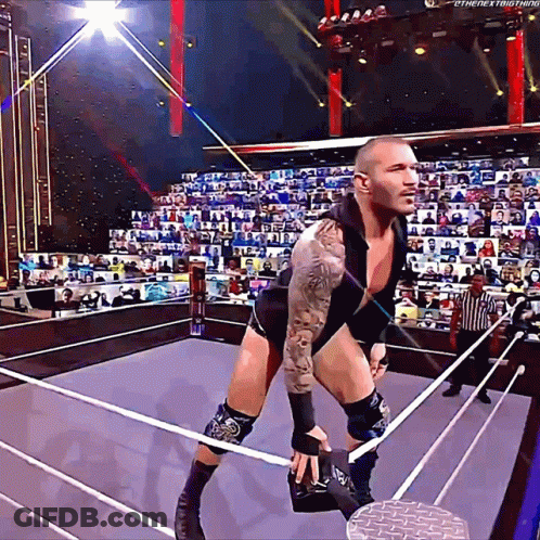 A Wrestler Is Standing In A Ring With A Referee In The Background GIF