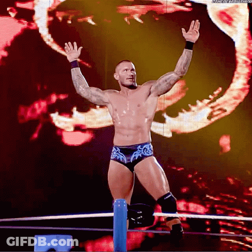 A Wrestler Is Standing In A Ring With His Arms In The Air And A Screen Behind Him That Says Wrestling GIF