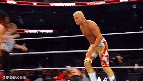 A Wrestler Is Standing In A Wrestling Ring With A Referee In The Background . GIF