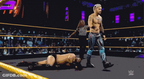 A Wrestler Is Standing In A Wrestling Ring With A Referee GIF