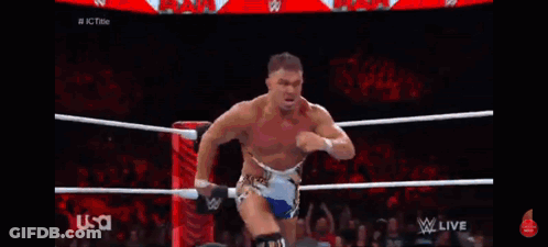 A Wrestler Is Standing In The Middle Of A Wrestling Ring While Another Wrestler Is Kneeling Down . GIF