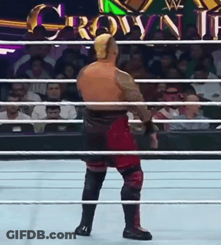 A Wrestler Is Standing In The Middle Of A Wrestling Ring With A Crowd Watching . GIF