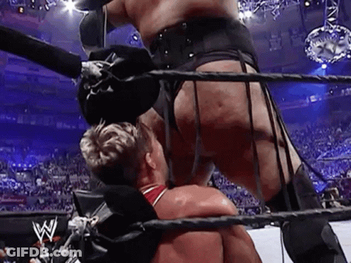 A Wrestler Is Standing On Top Of Another Wrestler In A Boxing Ring . GIF