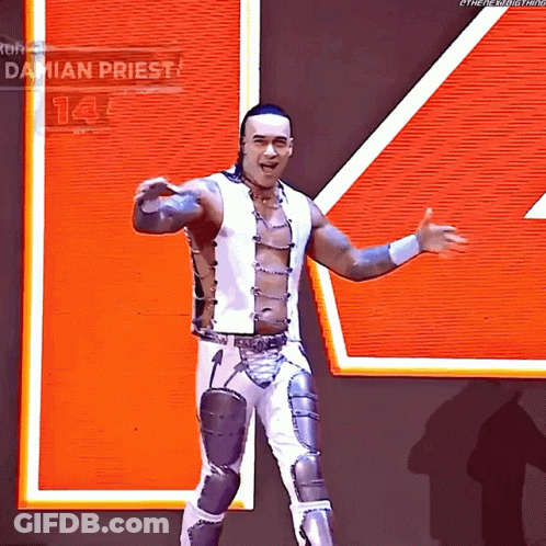 A Wrestler Named Damian Priest Stands In Front Of An Orange Sign GIF