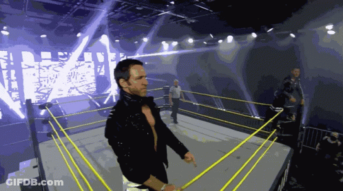A Wrestler Stands In A Wrestling Ring With A Large Screen Behind Him That Says Wrestling GIF