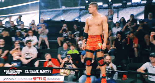 A Wrestler Stands In Front Of A Crowd With A Sign That Says Saturday March 1 On It GIF