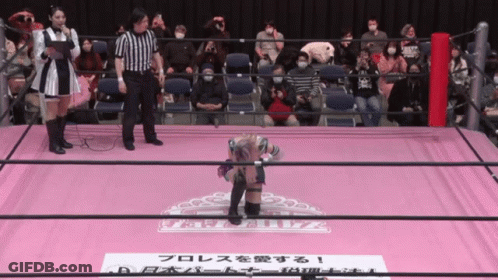 A Wrestler Stands On A Pink Mat With A Sign That Says ' A ' On It GIF