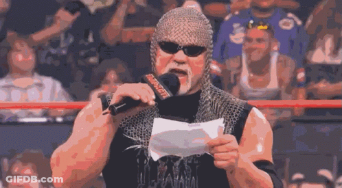 A Wrestler Wearing A Chain Mail Helmet Holds A Piece Of Paper In Front Of A Microphone That Says WWE GIF
