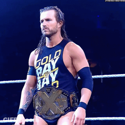 A Wrestler Wearing A Gold Bay Bay Shirt Stands In The Ring GIF