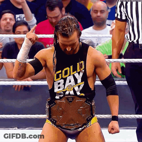 A Wrestler Wearing A Gold Bay Shirt Stands In The Ring GIF