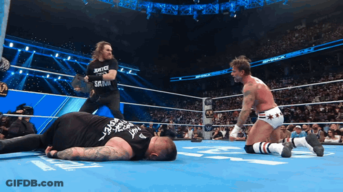 A Wrestler Wearing A Shirt That Says Justice And Sanity Is Standing Next To Another Wrestler GIF
