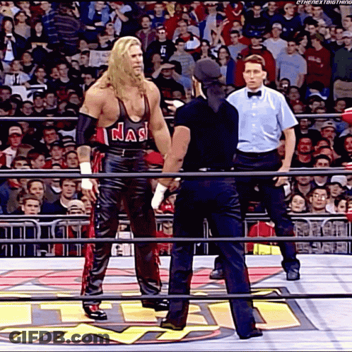 A Wrestler Wearing A Tank Top That Says Nas Is Standing In A Ring With A Referee GIF