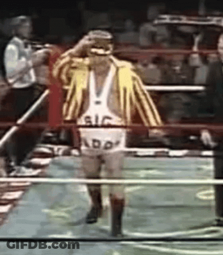 A Wrestler Wearing A Yellow And White Striped Jacket And Shorts With The Word Add On Them Walks Through A Ring GIF