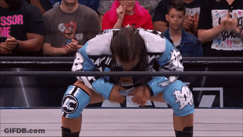 A Wrestler Wearing Knee Pads With Ac On Them Is Kneeling Down In Front Of A Crowd GIF