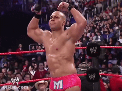 A Wrestler Wearing Pink Shorts With The Letter M On Them Stands In A Wrestling Ring GIF