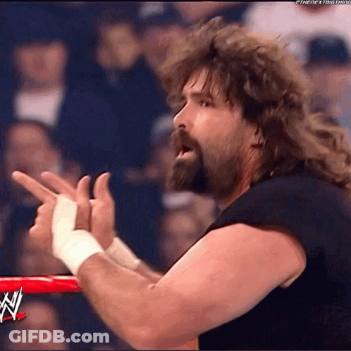 A Wrestler With A Beard And Long Hair Is Pointing His Fingers In The Air GIF
