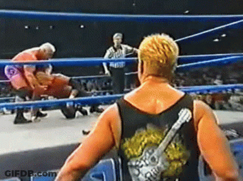 A Wrestler With A Guitar On His Back Is Standing In A Wrestling Ring . GIF