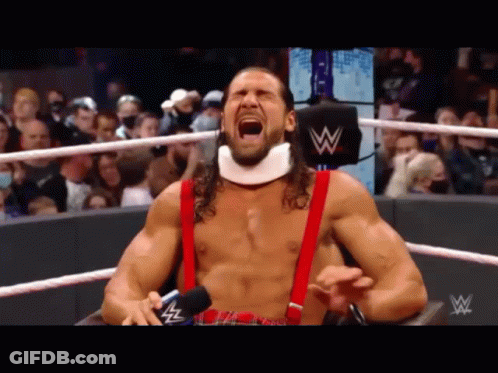A Wrestler With A Neck Brace And Suspenders Is Screaming In A Ring . GIF