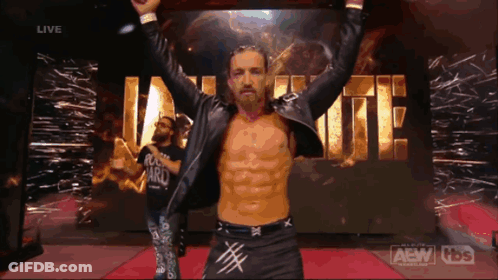 A Wrestler With His Arms In The Air In Front Of A Sign That Says Aew GIF