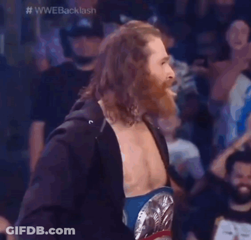A Wrestler With Long Hair And A Beard Is Wearing A Wrestling Belt . GIF