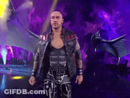 A Wrestler With Wings Is Walking On A Stage In Front Of A Dragon GIF