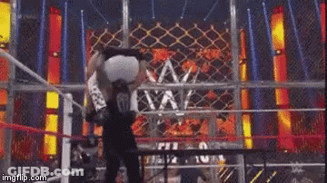 A Wrestling Match Is Being Held In A Ring With A Fence In The Background . GIF