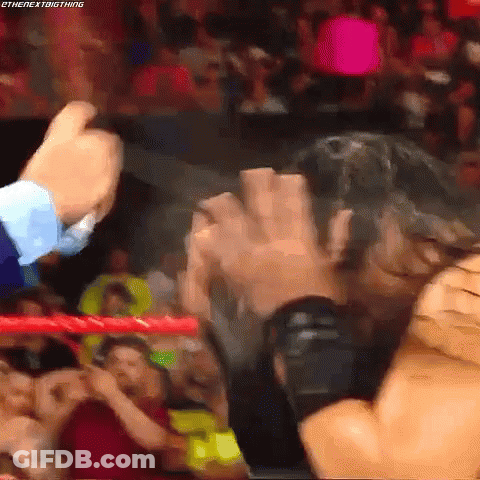 A Wrestling Match Is Going On In A Crowded Stadium And A Man Is Holding Another Man 'S Hand . GIF