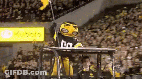 A Yellow And Black Mascot Is Sitting On Top Of A Tractor Holding A Flag . GIF
