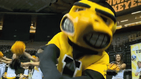 A Yellow And Black Mascot Stands In Front Of Cheerleaders And A Sign That Says Keys GIF
