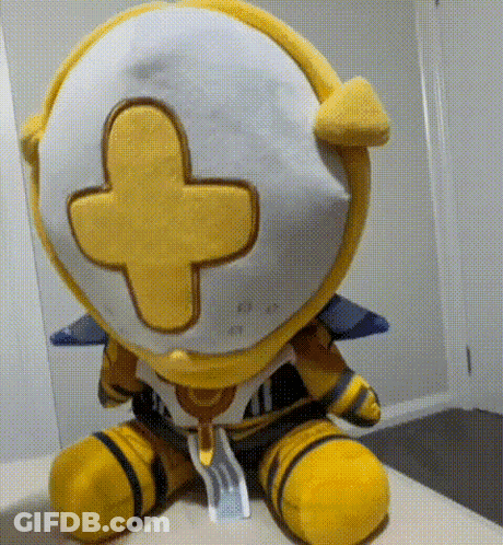 A Yellow And White Stuffed Animal With A Yellow Cross On Its Head Is Sitting On A Bed . GIF