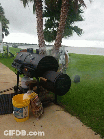 A Yellow Bucket With The Word Fire On It Sits On A Sidewalk Next To A Grill GIF