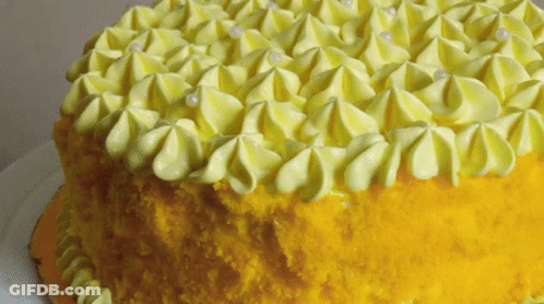 A Yellow Cake With Yellow Frosting And White Pearls GIF