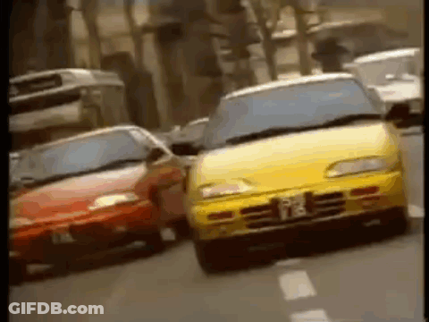 A Yellow Car And A Red Car Are Driving Down A City Street . GIF