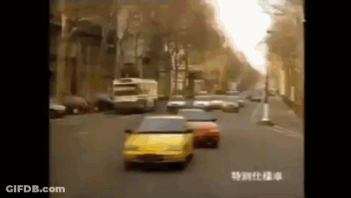 A Yellow Car Is Driving Down A Busy City Street . GIF