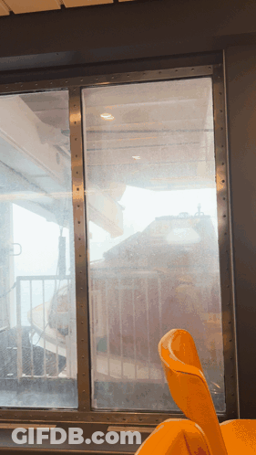 A Yellow Chair Sits In Front Of A Window Looking Out GIF