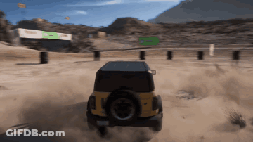 A Yellow Jeep Is Driving Down A Dirt Road With A Green Sign In The Background GIF