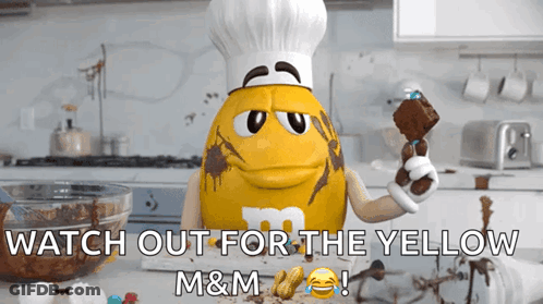 A Yellow M&m Wearing A Chef Hat Is Holding A Brownie GIF