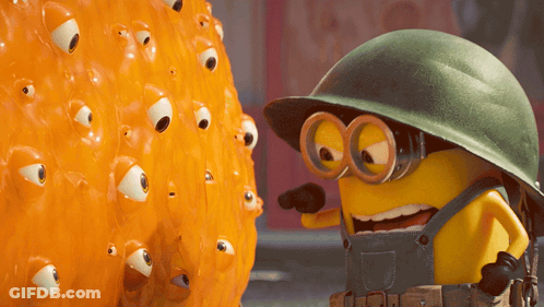 A Yellow Minion Wearing Overalls And A Helmet Is Pointing At An Orange Object With Eyes On It GIF