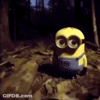 A Yellow Minion With Big Eyes Is Standing In A Dark Forest . GIF