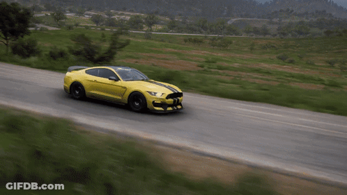 A Yellow Mustang Is Driving Down A Road With Grass On The Side GIF